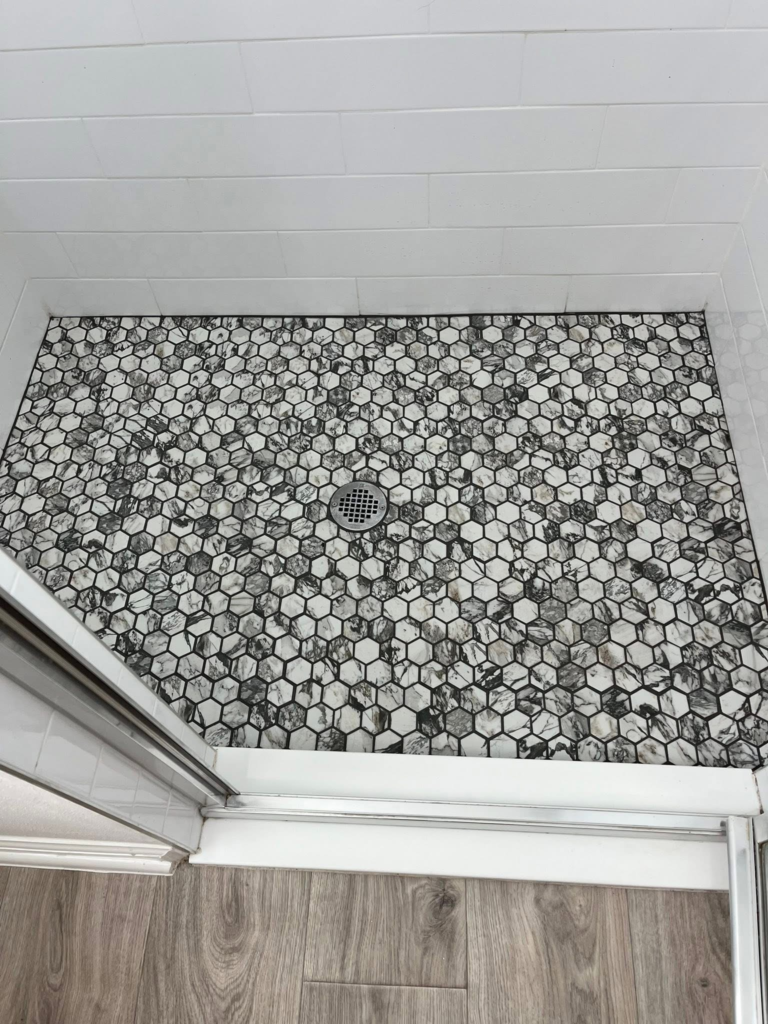 Precision tile work on a custom-sloped shower pan featuring a modern, high-contrast monochrome hexagon mosaic layout.