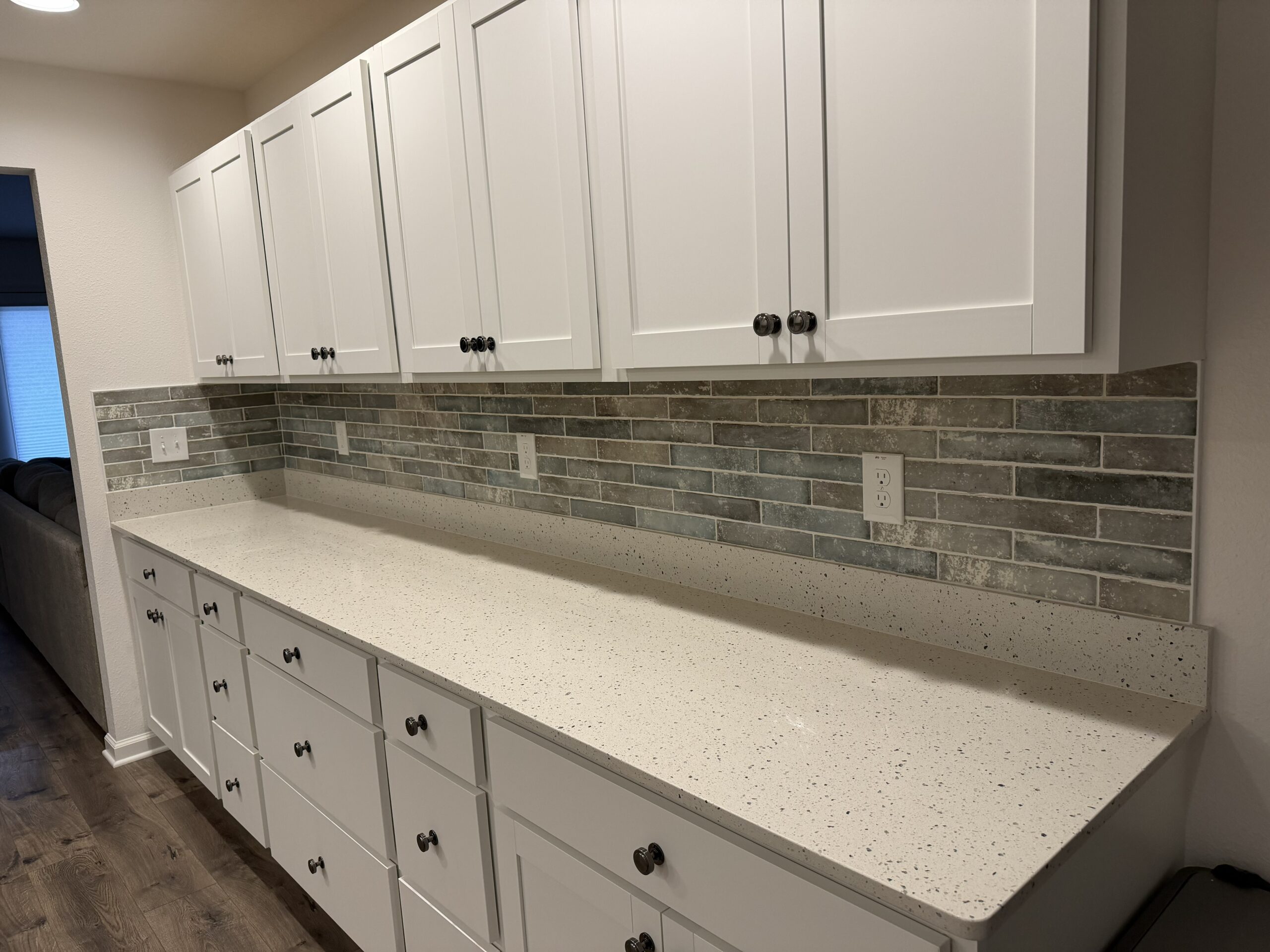 Classic earth-toned plank tile backsplash installation for a long kitchen counter with white cabinetry and quartz countertops.