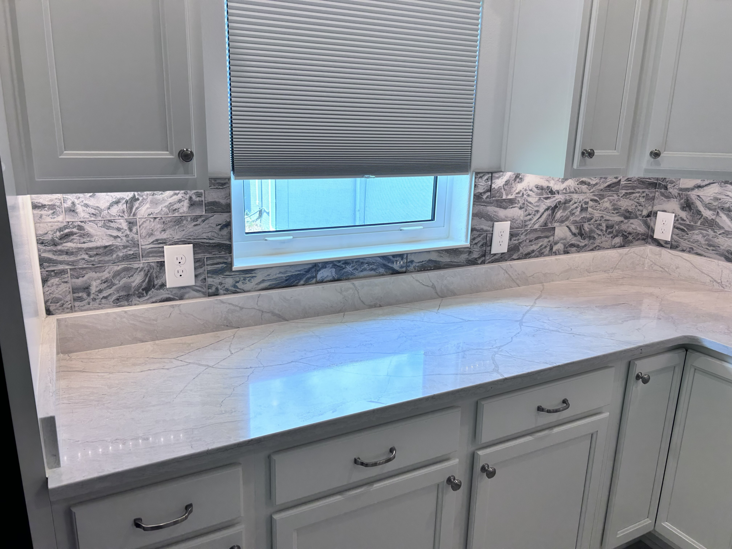 Elegant stone-swirl tile backsplash paired with marble countertops and light grey cabinetry for a seamless, high-end look.
