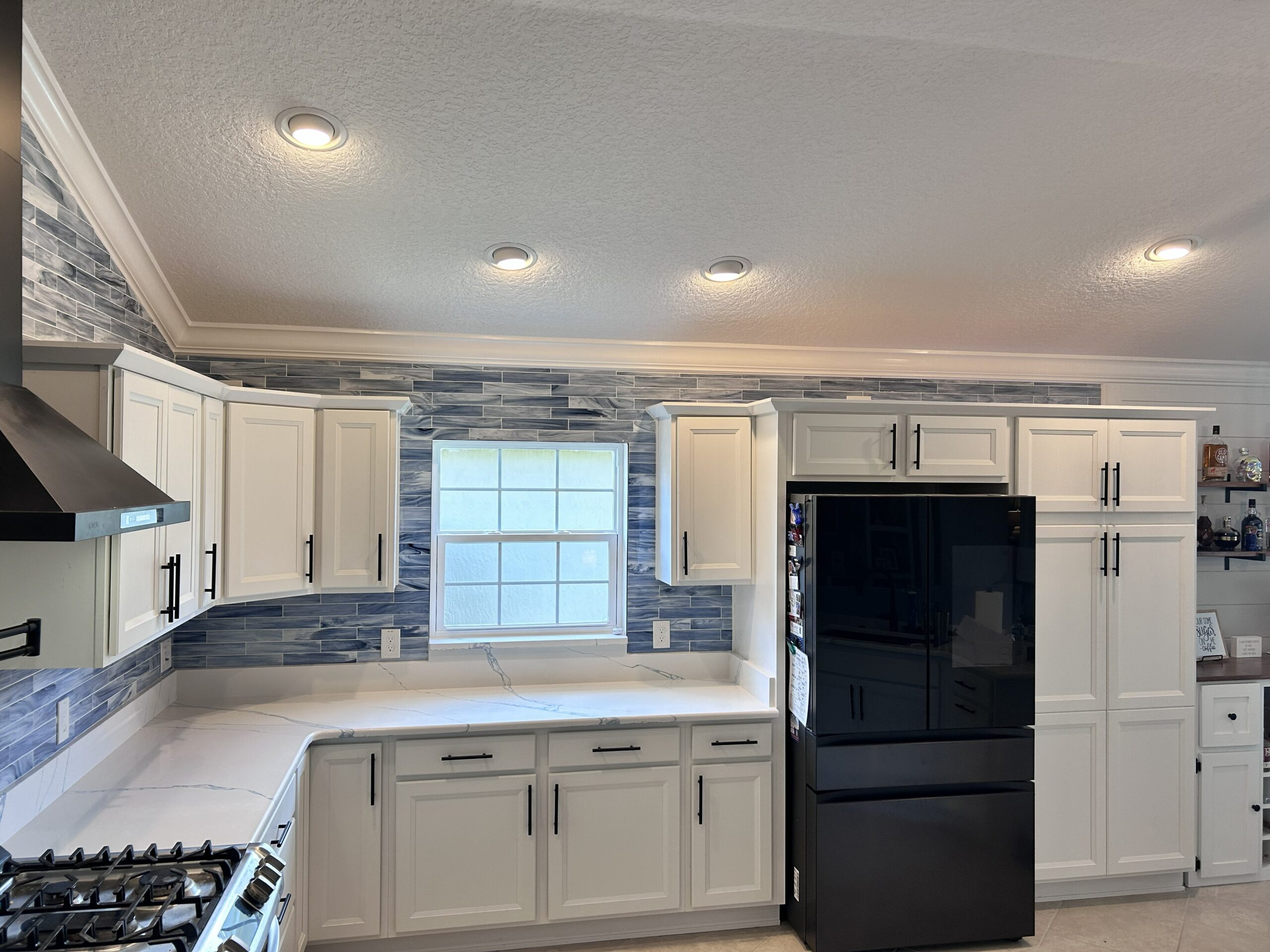 Custom kitchen tile backsplash in vibrant blue glass, expertly cut to fit around windows and cabinetry in The Villages, FL.