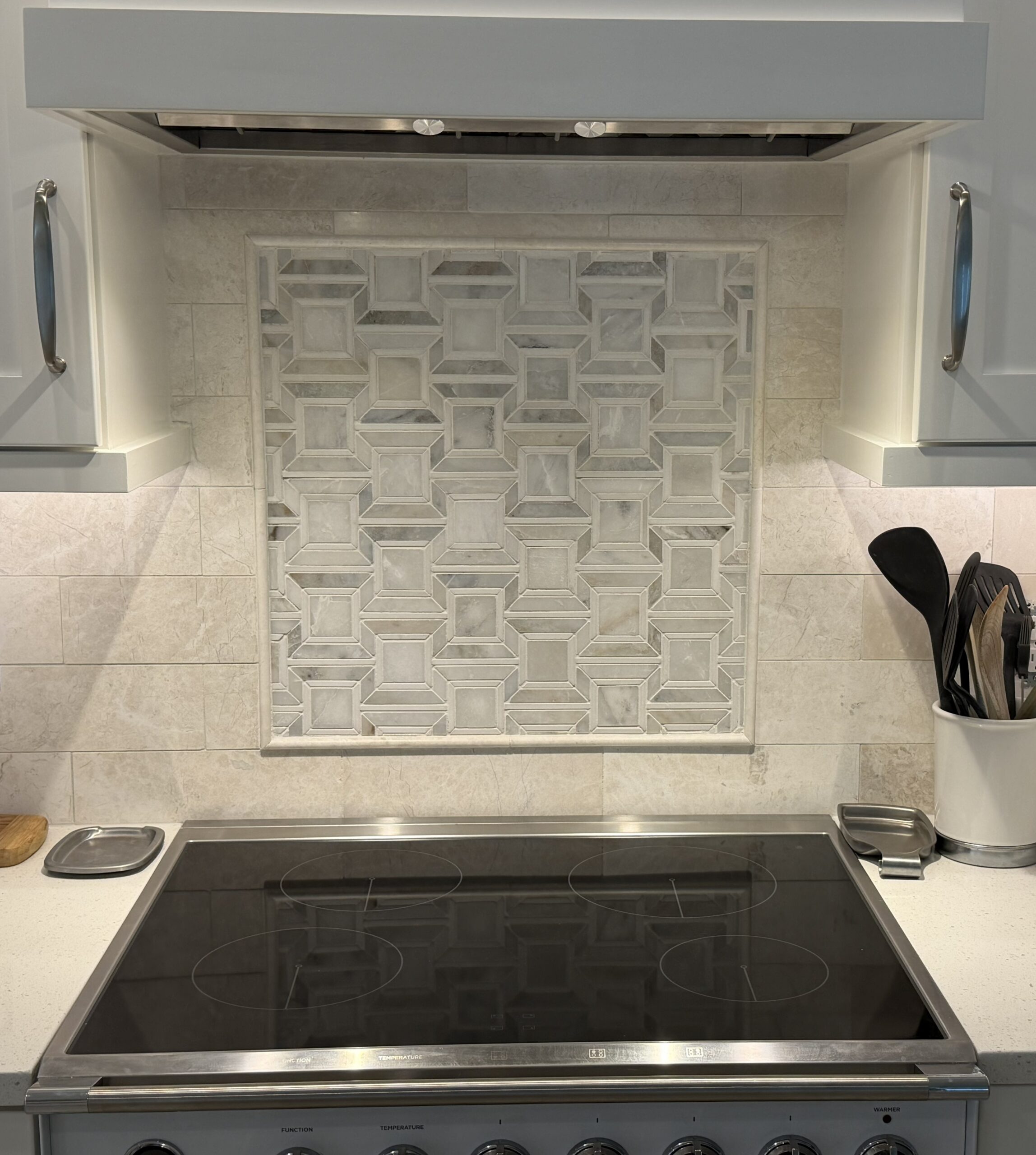 Custom-framed marble geometric mosaic backsplash inset feature behind a kitchen range cooktop.