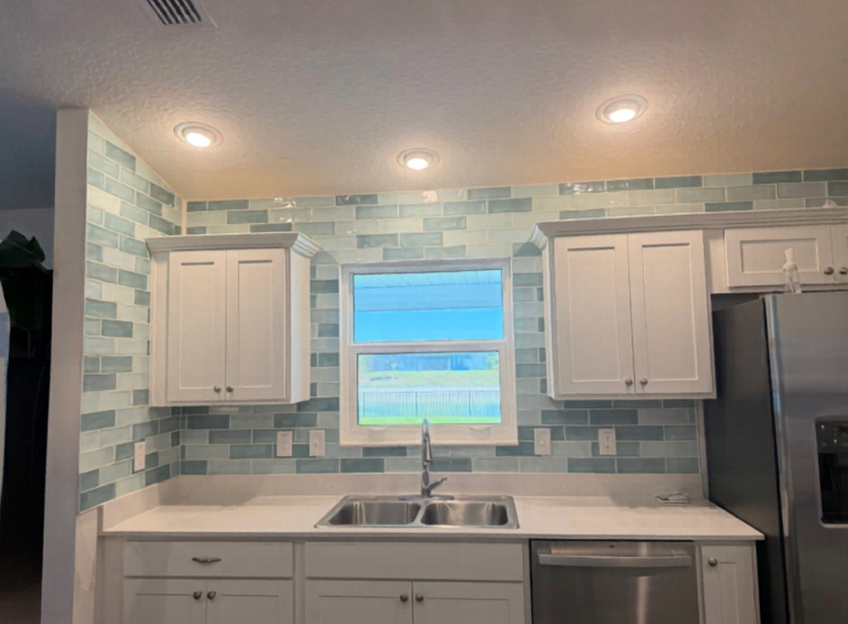 Coastal-inspired seafoam green glass subway tile backsplash installed from counter to ceiling, featuring precision cuts around kitchen windows and cabinetry.