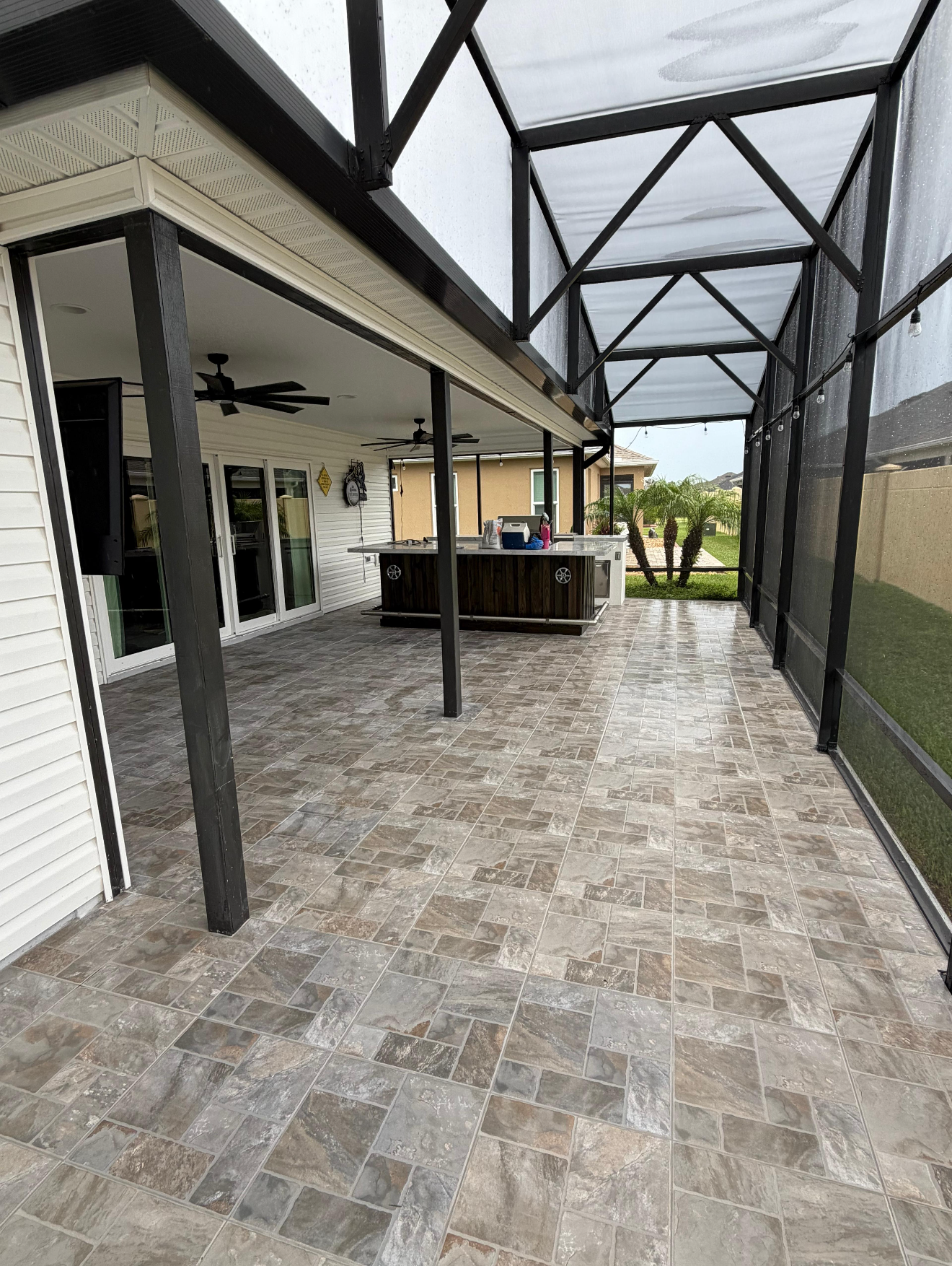 This custom porcelain tile installation transforms this screened lanai into a spacious, inviting outdoor living area. The natural stone-look tile complements the outdoor kitchen, entertainment space, and surrounding architecture while providing a durable, low-maintenance surface designed for Florida living.
